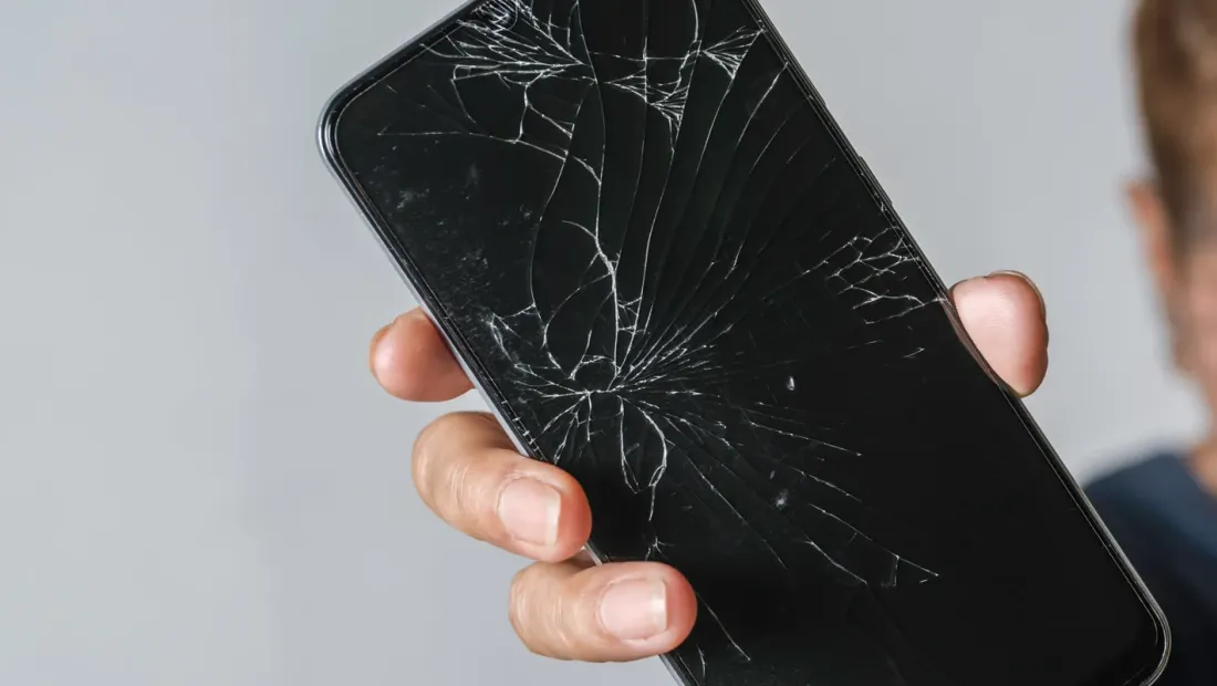 Woman holding a phone with a cracked screen on a grey table
