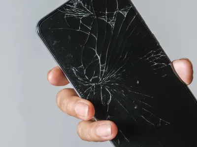 Woman holding a phone with a cracked screen on a grey table
