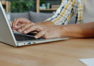 Hands typing on a laptop keyboard at a wooden desk