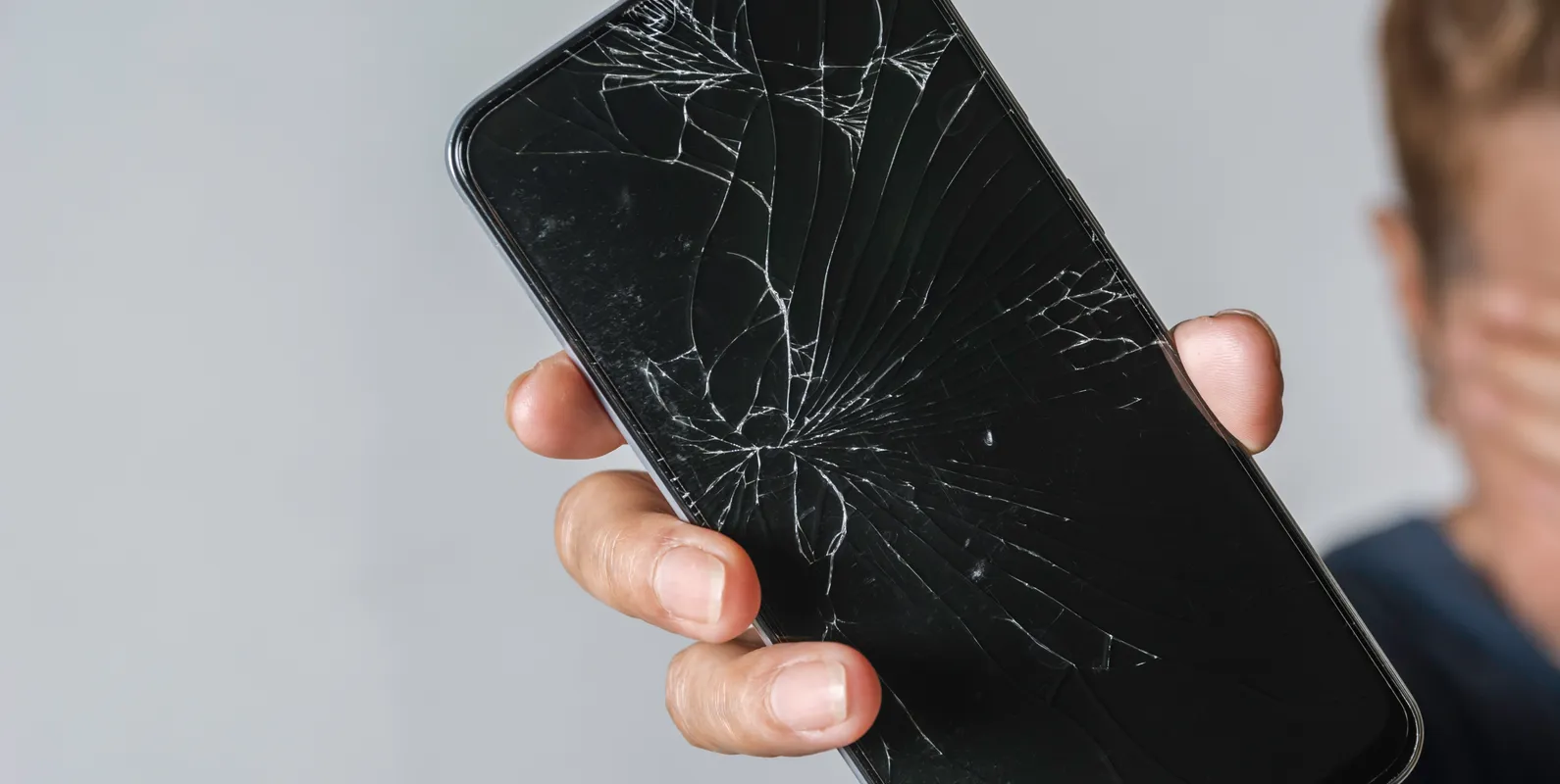 Woman holding a phone with a cracked screen on a grey table