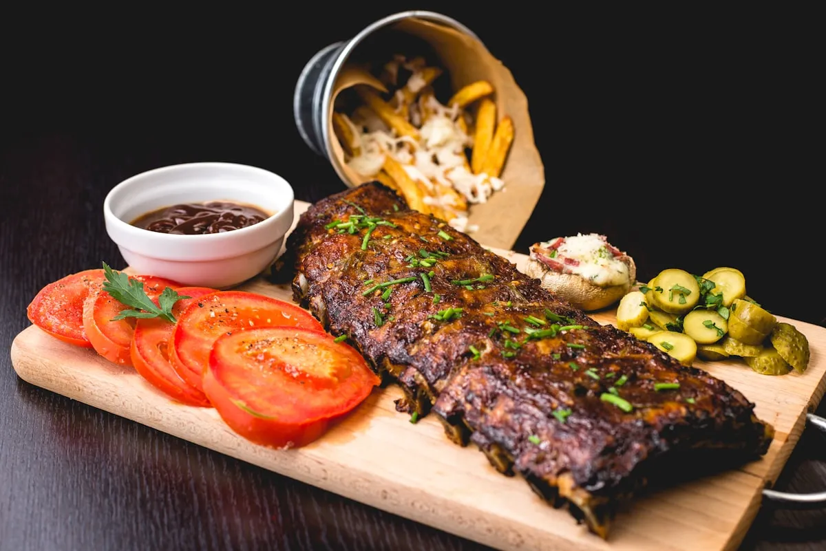 Grilled ribs platter with sides on a wooden cutting board at a restaurant