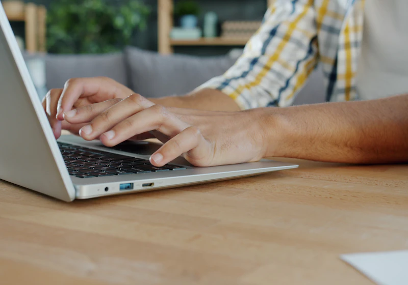 Hands typing on a laptop keyboard at a wooden desk